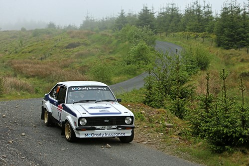 Fintan McxGrady's vitnage ford escort rally car takes a corner in a mountainous forest track.